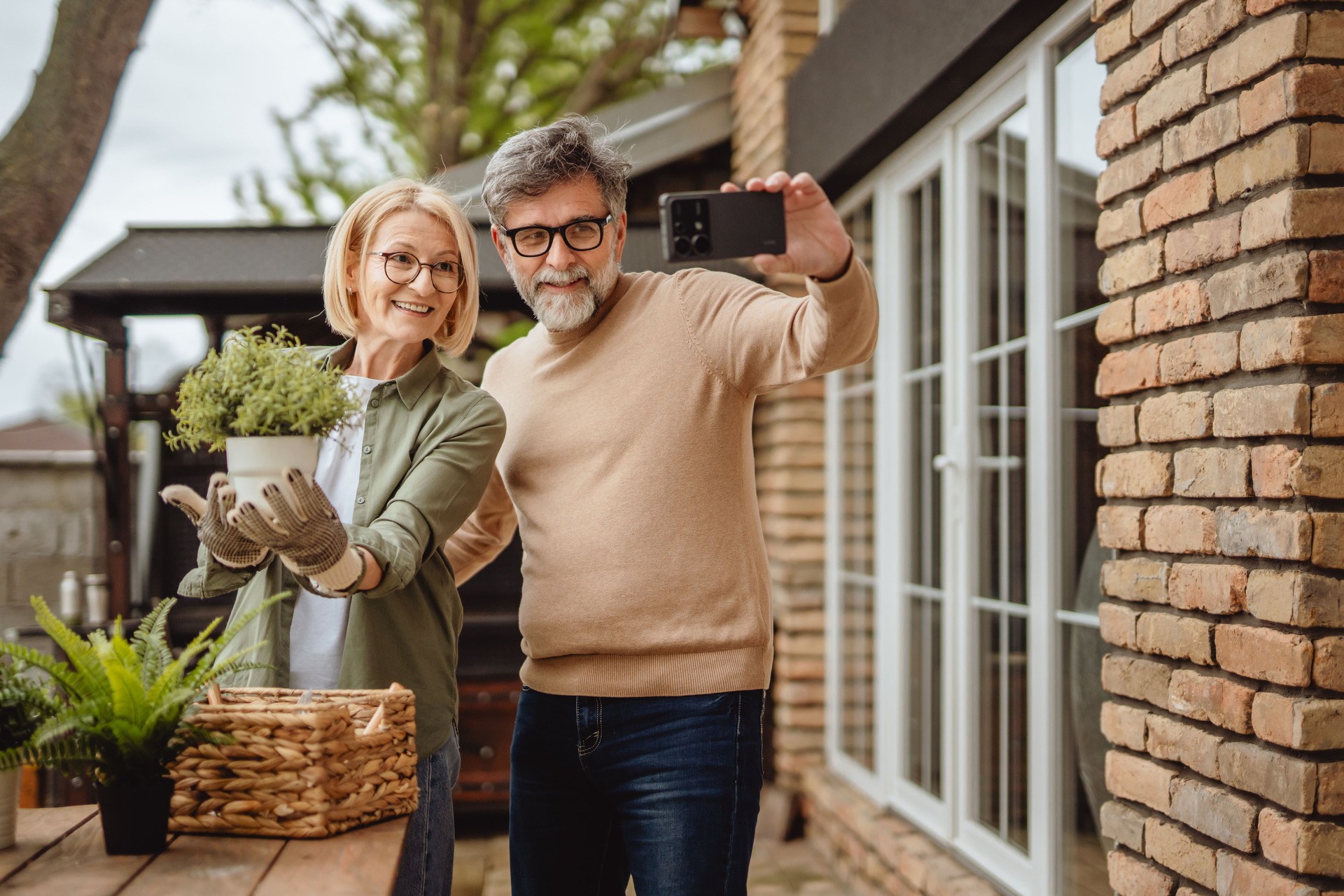 Des personnes âgées heureuses font un autoportrait avec des plantes en pot devant la maison