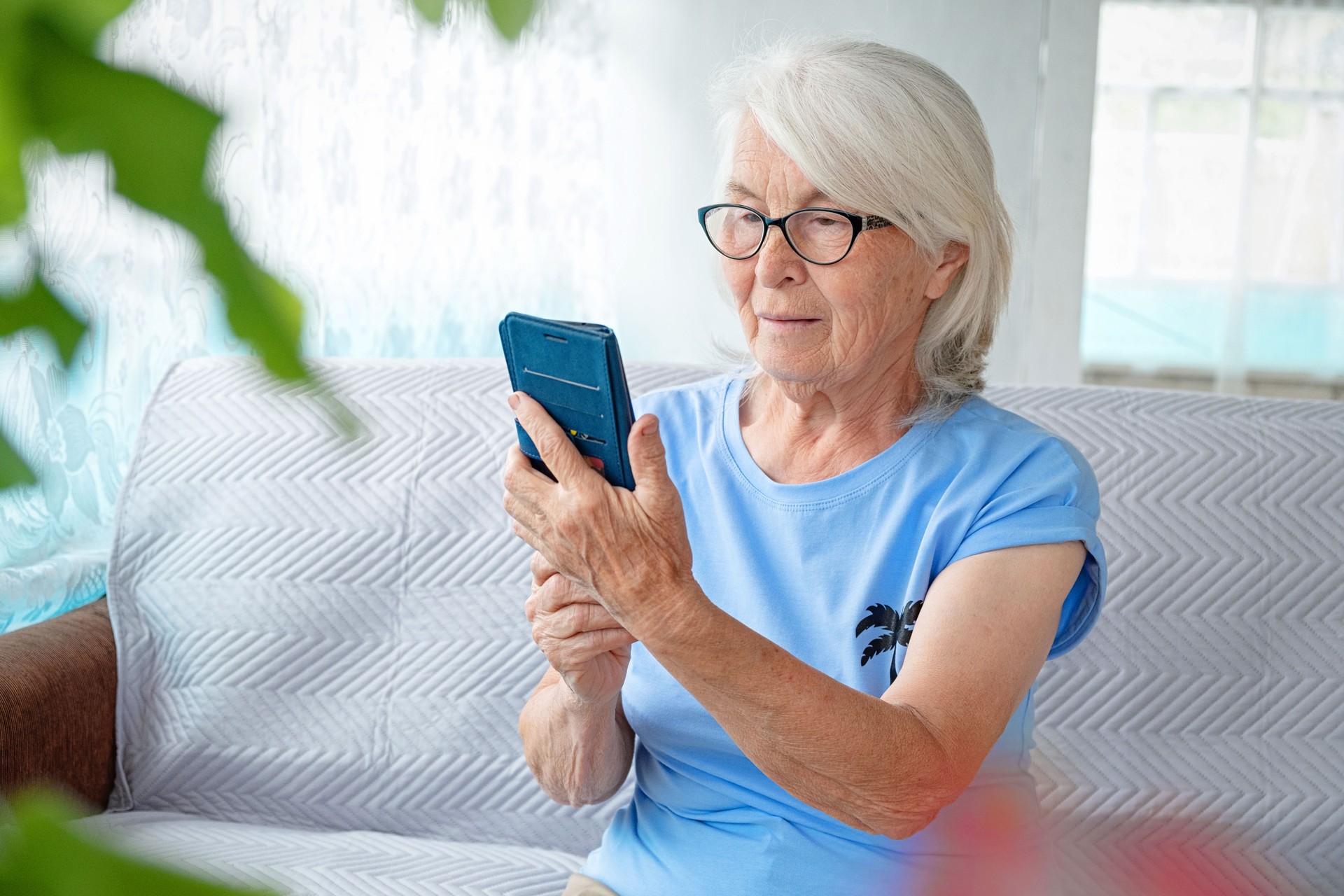 Portrait en gros plan d’une femme senoir avec des lunettes et des cheveux gris assis sur un canapé et tenant un smartphone. Le concept d’utilisation des technologies modernes pour les personnes âgées